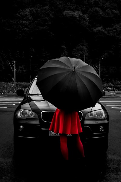 站在车前，黑伞下穿着红色喇叭裤的女子